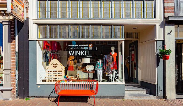 Vooraanzicht van winkel Terre des Hommes met een rood bankje voor het raam